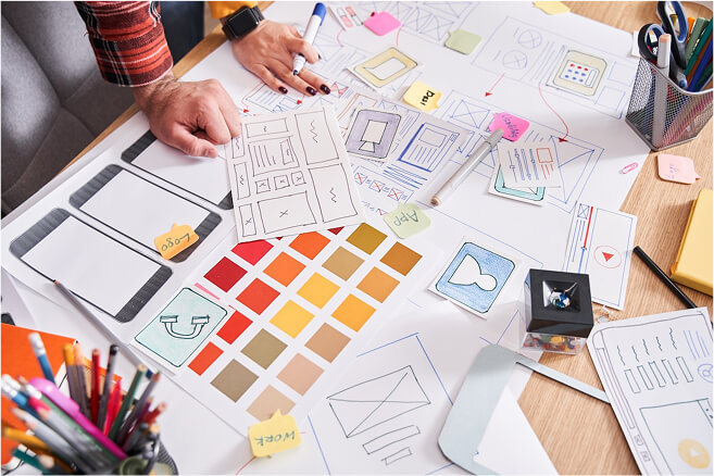 Placeholder Image (1) (1) Hands on a table with a bunch of designs on paper