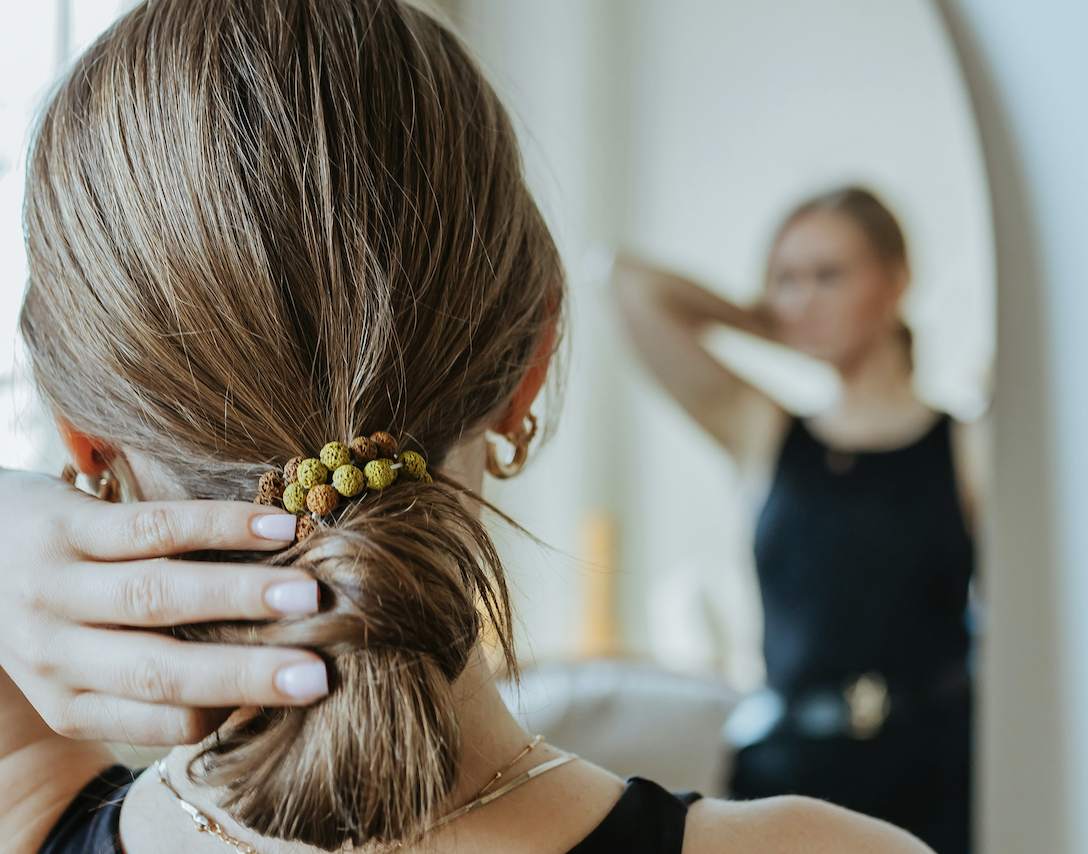 girl looking in the mirror with her hand behind her head and her hair in a bun showing who we are and who we want to be