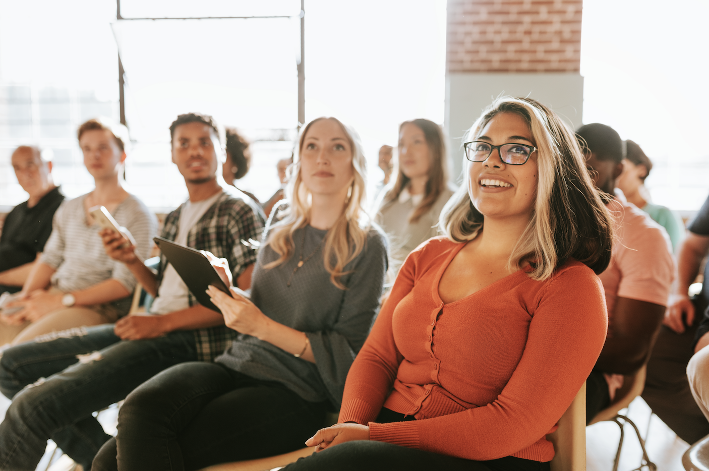 Group of people sitting in rows of chairs smiling at the front of the room during training session to show participation