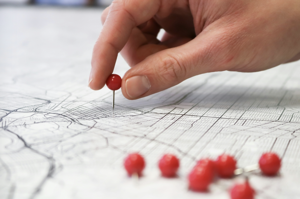 hand putting a red pin on a map with a pile of pins next to him